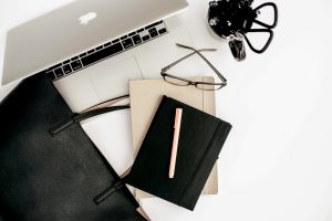 Flat lay of a black and beige planner with pen, laptop and glasses. Ideal tools for organized Allied Health Students.